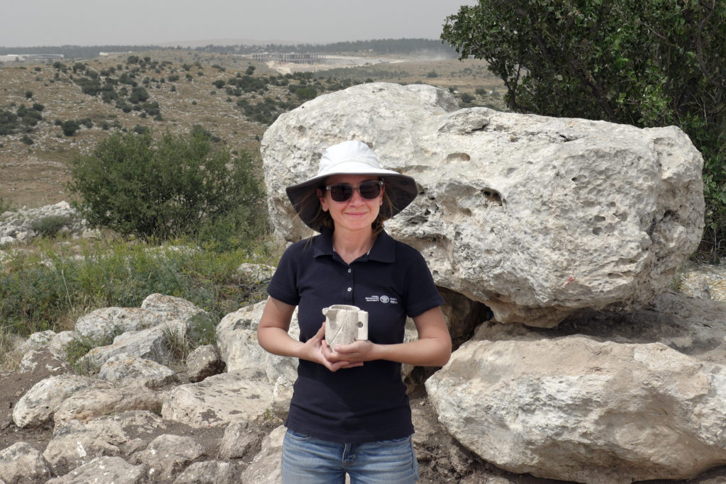 . ארכיאולוגית רשות העתיקות, ג'ני מרכוס, מחזיקה ספל אבן מימי הבית השני שהתגלה בבית האחוזה. צילום: אברהם טנדלר