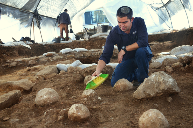 כפיר ארביב, מנהל החפירה מטעם רשות מהעתיקות, מנקה את אחת מאבני הקלע. צילום: יולי שוורץ