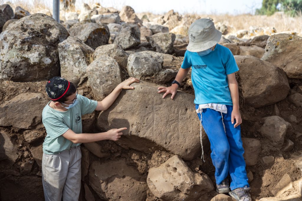 ילדים מחיספין המתנדבים בחפירה, מצביעים על הדמויות שחרותות על האבן. צילום: יניב ברמן