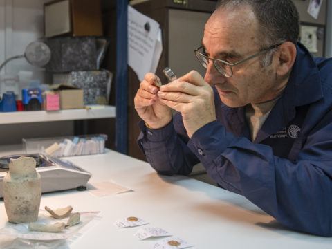 דר' רוברט קול בוחן את אחד המטבעות שנמצאו בפכית. צילום שי הלוי רשות